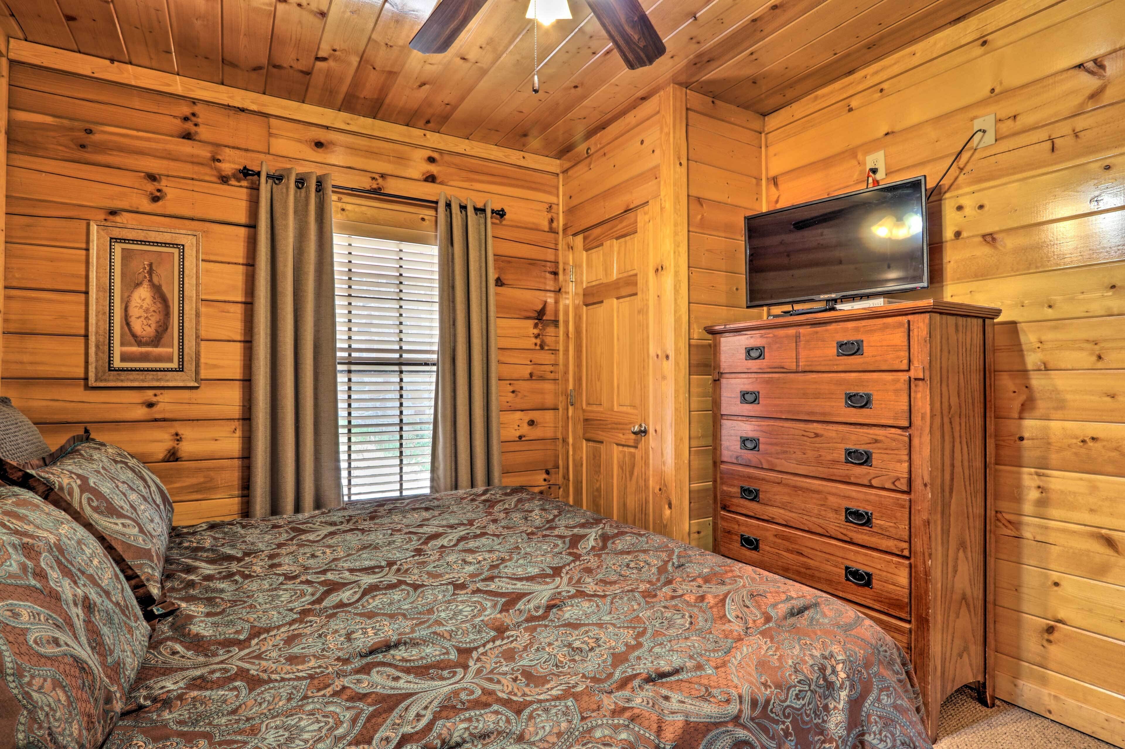 Een kamer met houten lambrisering, een bed, een dressoir, een televisie en een raam met jaloezieën.