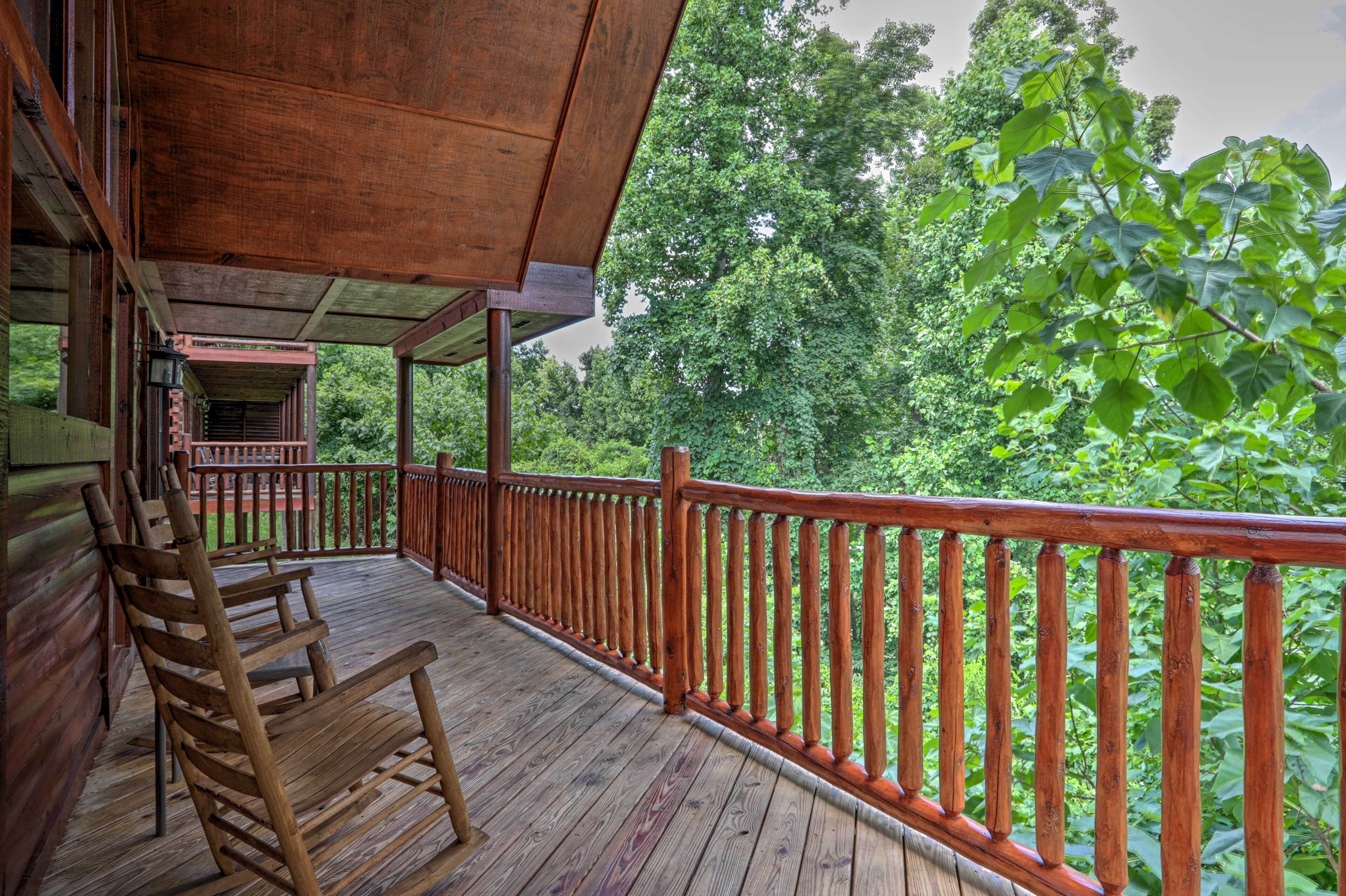 A wooden deck with a railing, wooden chairs, and a view of a forested area.