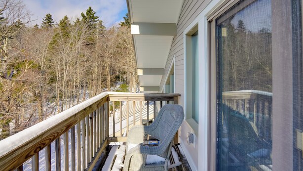 A balcony with a wicker chair, a wooden railing, and a view of a forested area. - Bromley Mountain Escape w/ 2 Balconies: Hike & Ski (Peru)
