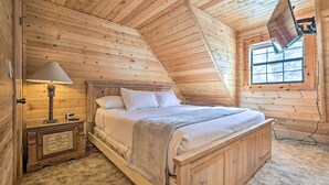 Un dormitorio de cabaña de madera con cama, mesita de noche, lámpara y ventana.