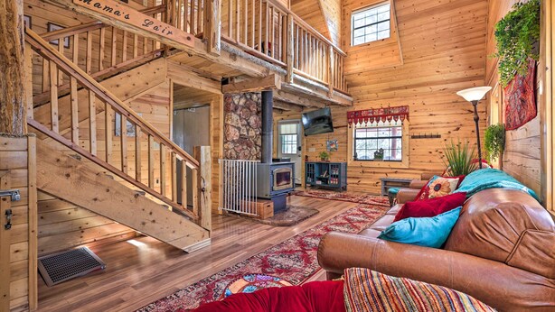 Interior de una cabaña de madera con escalera, chimenea, sofá y televisor.