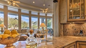 A kitchen with granite countertops, a large bowl of lemons, a bottle of liquor, and a dining area with a sofa and lamps. - Lavish Paradise Valley Home w/ Sports Court & Pool (Paradise Valley)