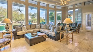A spacious living room with a sectional sofa, ottoman, and two side tables with lamps. Large windows provide a view of the outdoors. - Lavish Paradise Valley Home w/ Sports Court & Pool (Paradise Valley)