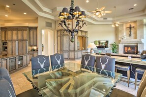 A spacious living room with a glass-top dining table surrounded by chairs, a chandelier, and a fireplace.