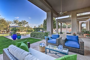 Un espace extérieur aménagé en terrasse, avec des meubles en osier, une table en verre et une vue sur une piscine et la verdure.