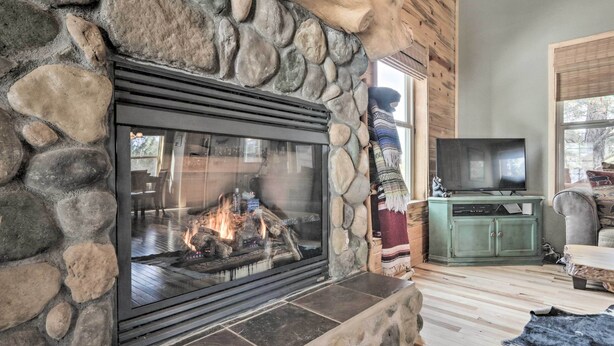 A stone fireplace with a TV on top, a wooden ceiling, and a stone wall. - Fire Pit + Game Room: Heber-overgaard Cabin! (Overgaard)