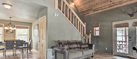 A spacious living room with a wooden staircase, a gray sofa, and a dining area with a table and chairs.