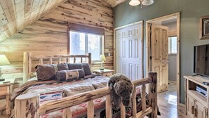 A cozy bedroom with a wooden ceiling, a bed with a patterned blanket, a dog resting on a wooden chair, and a television on a wooden stand. - Fire Pit + Game Room: Heber-overgaard Cabin! (Overgaard)
