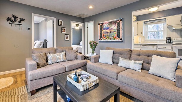Ein modernes Wohnzimmer mit zwei grauen Sofas, einem Couchtisch und einem durchgehenden Gang sichtbaren Küchenbereich.