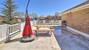 A concrete patio with a picnic table and umbrella, a brick building, and a white fence. - Downtown Canandaigua Apt: 1 Mi to Lake & Pier! (Canandaigua)