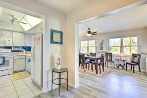 A kitchen with white cabinets, a microwave, and a refrigerator. There is a dining area with a table and chairs, and a ceiling fan. - Venice Home w/ Private Pool, 7 Mi to Beach! (Venice)