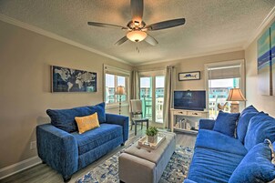 A living room with a blue sofa, a beige ottoman, and a ceiling fan.