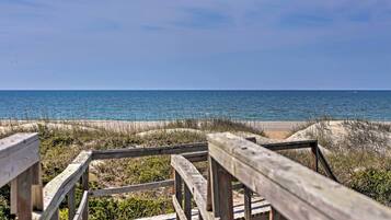 A wooden boardwalk leading to a beach with sand dunes and the ocean in the background.