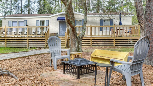 A mobile home with a deck, outdoor seating, and a tree in the foreground.