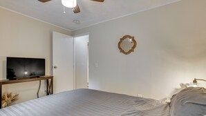A bedroom with a bed, a television on a stand, a door, and a wall-mounted mirror.