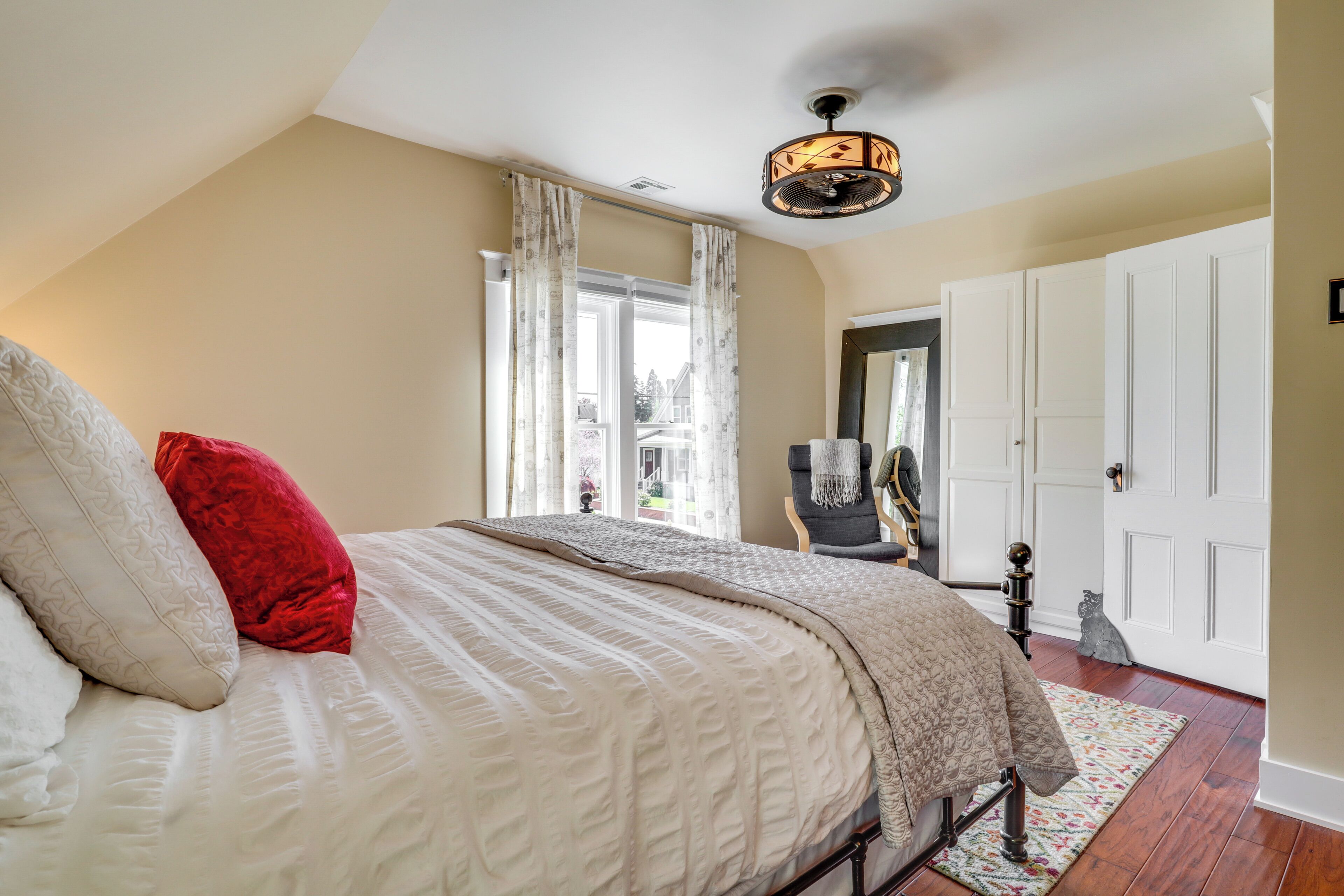 Une chambre avec un grand lit, un ventilateur de plafond et une vue sur l’extérieur par une fenêtre munie de rideaux.