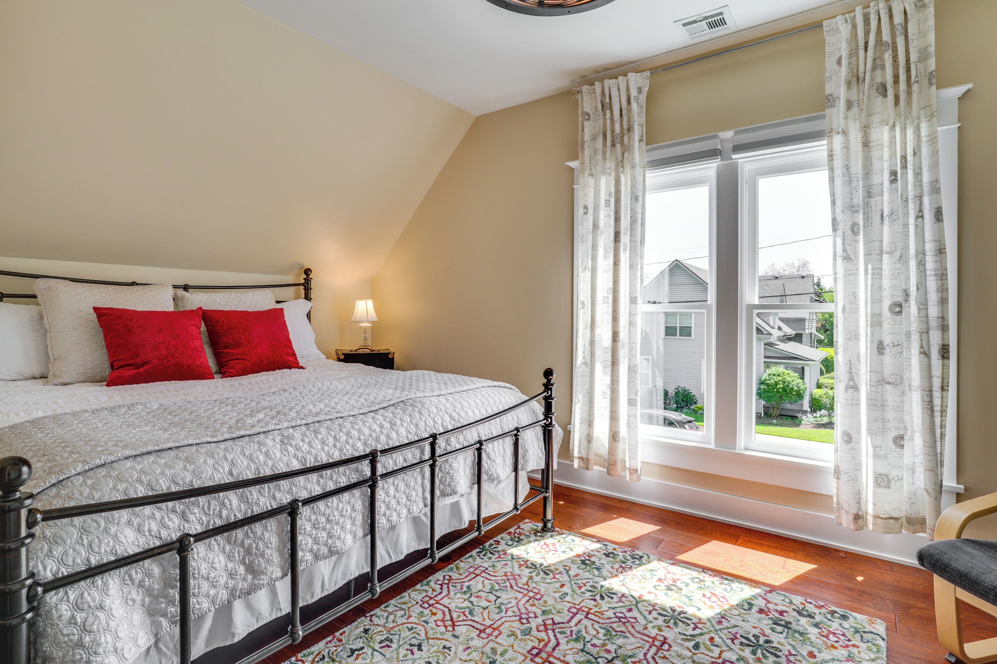 A bedroom with a bed, a nightstand, a window with curtains, and a view of the outside.