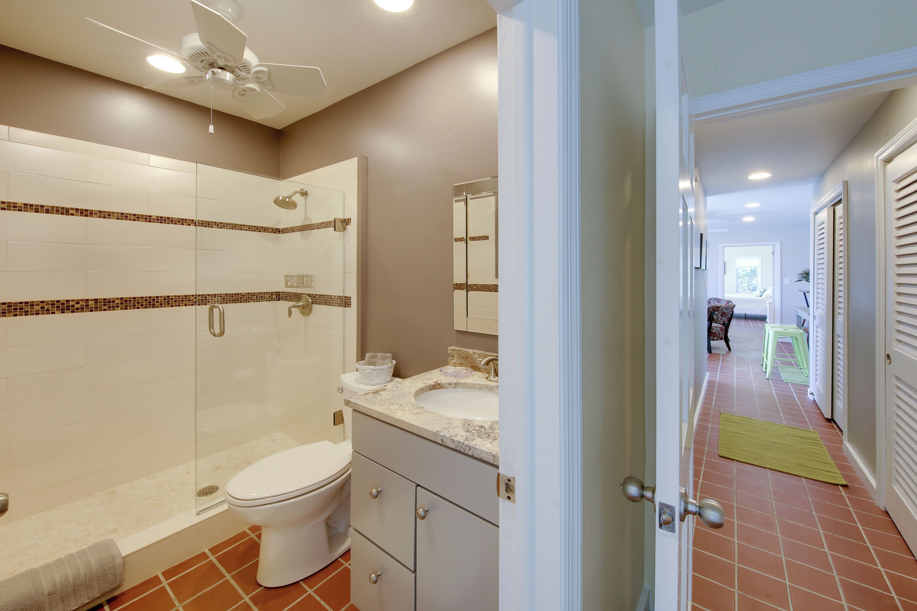 A bathroom with a glass shower enclosure, a toilet, a sink with a marble countertop, and a mirror above the sink.