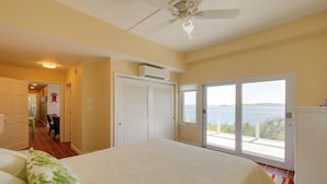 A bedroom with a large bed, a ceiling fan, and a view of the sea through a sliding glass door. - 'sea La Vie' - Waterfront St Thomas Escape w/ Pool (St. Thomas)
