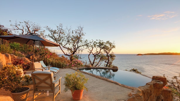 A private pool area with lounge chairs and a pergola, overlooking a calm sea and rocky terrain. - 'sea La Vie' - Waterfront St Thomas Escape w/ Pool (St. Thomas)