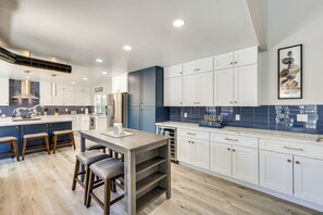 A modern kitchen with white cabinets, a central island with stools, and a blue backsplash.