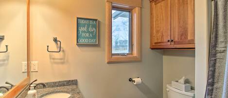 Un baño con lavamanos de encimera de granito, armarios de madera, una ventana y un inodoro.
