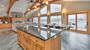A spacious kitchen with a large island, wooden beams, and large windows offering views of the outdoors. - Dock, Hot Tub & Game Room: Luxe Lake Latoka Home (Alexandria)