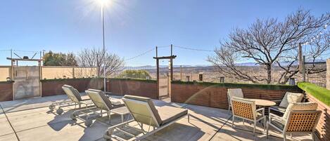 An outdoor patio with lounge chairs and a table, overlooking a scenic landscape.