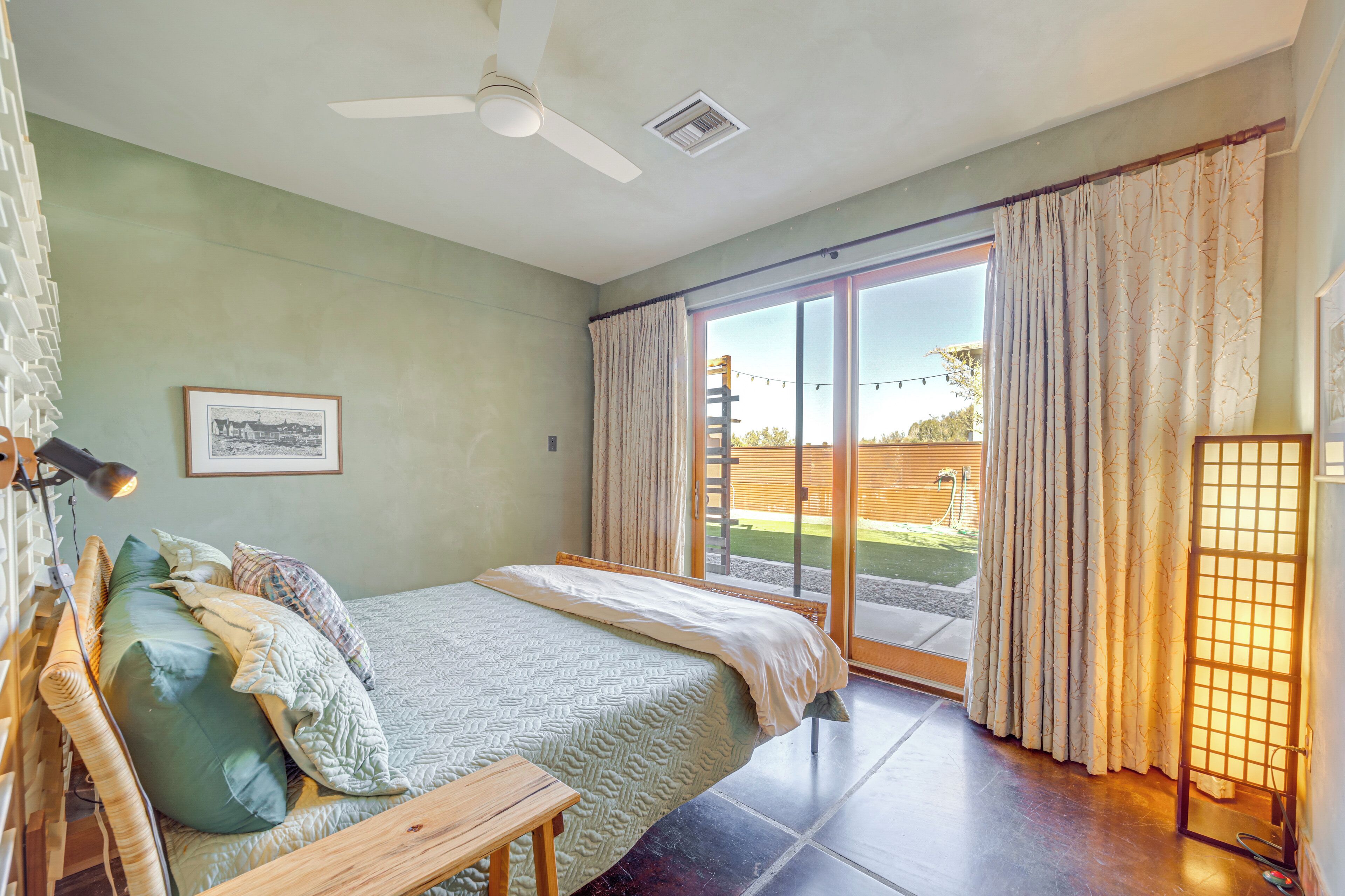 A bedroom with a bed, a bedside table, a ceiling fan, and a large sliding glass door leading to an outdoor area.