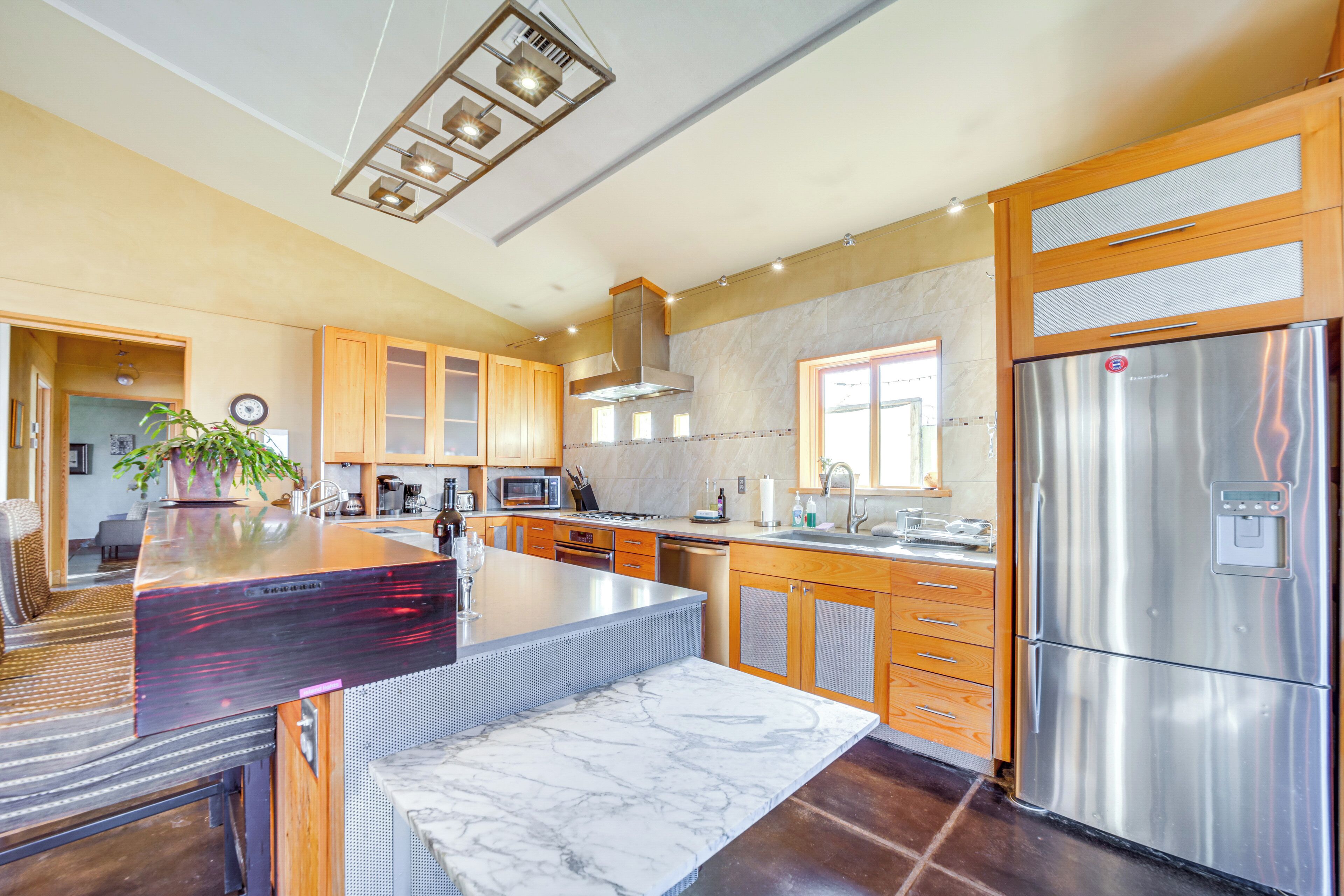 Une cuisine moderne avec des meubles en bois, un grand îlot central, des appareils en acier inoxydable et un plan de travail en marbre.