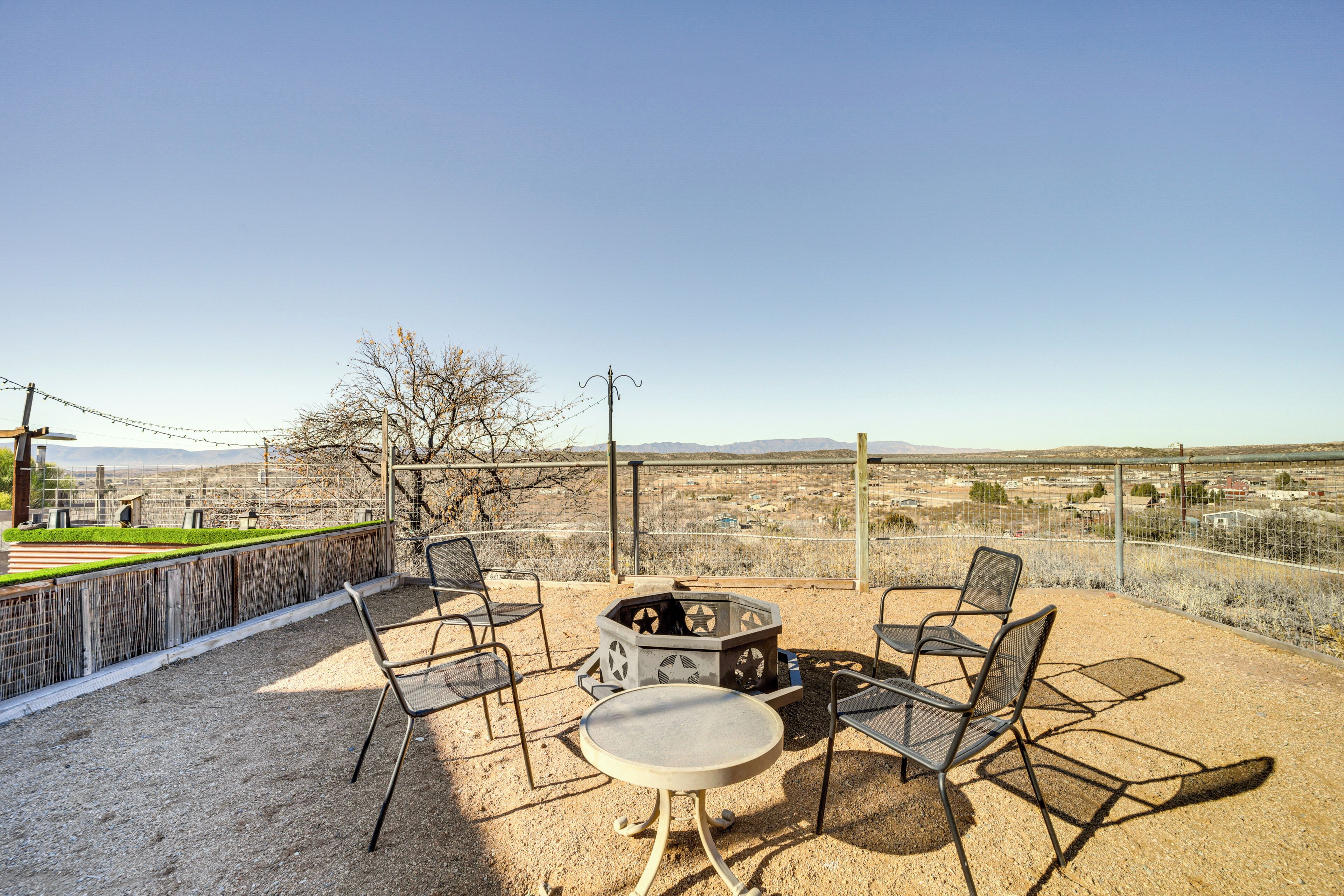 An outdoor patio with a round table and four chairs, a fire pit, and a view of a cityscape and mountains.
