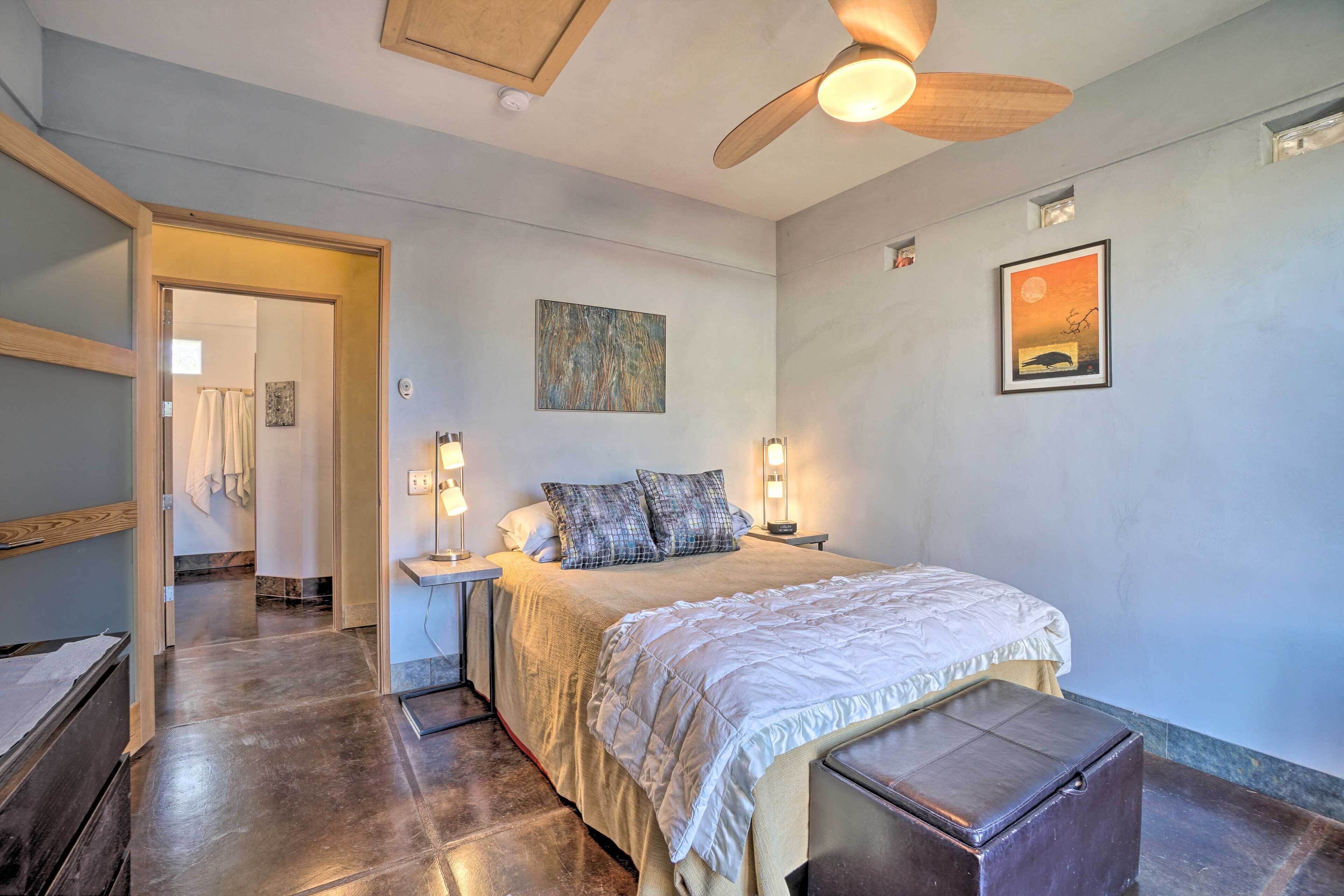 Une chambre à coucher avec un lit, des lampes de chevet, un ventilateur de plafond et des œuvres d’art accrochées aux murs.