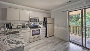 A modern kitchen with stainless steel appliances, a marble countertop, and a sliding glass door leading to a balcony. - Updated Wilmington Retreat ~ 2 Miles to Uncw! (Wilmington)