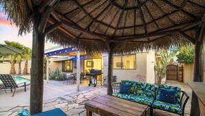 Un espace extérieur aménagé en terrasse, doté d’un toit de chaume, d’un sol en pierre et de différents espaces pour s’asseoir.