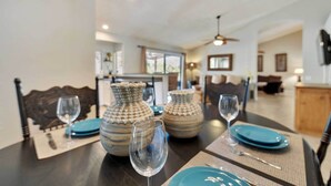 Une table à manger dressée avec de l’argenterie bleue et des verres à vin, entourée de vases décoratifs.