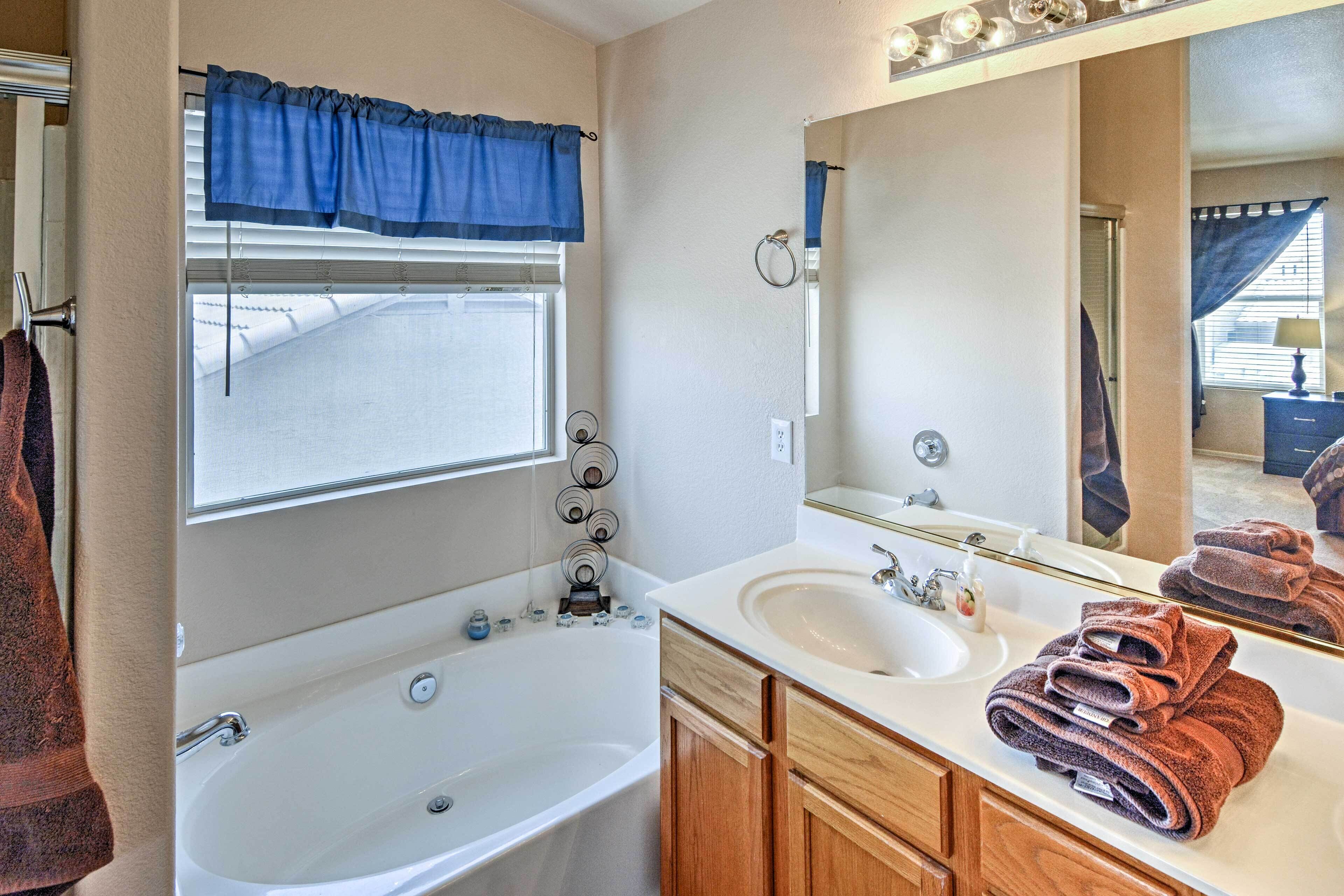 A bathroom with a bathtub, a sink, a mirror, and towels.