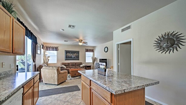 A kitchen with wooden cabinets, a granite countertop, and a built-in island. There is a dining area with a couch and a coffee table. - 2 Mi to Goodyear Ballpark! Home w/ Poolside Oasis (Goodyear)