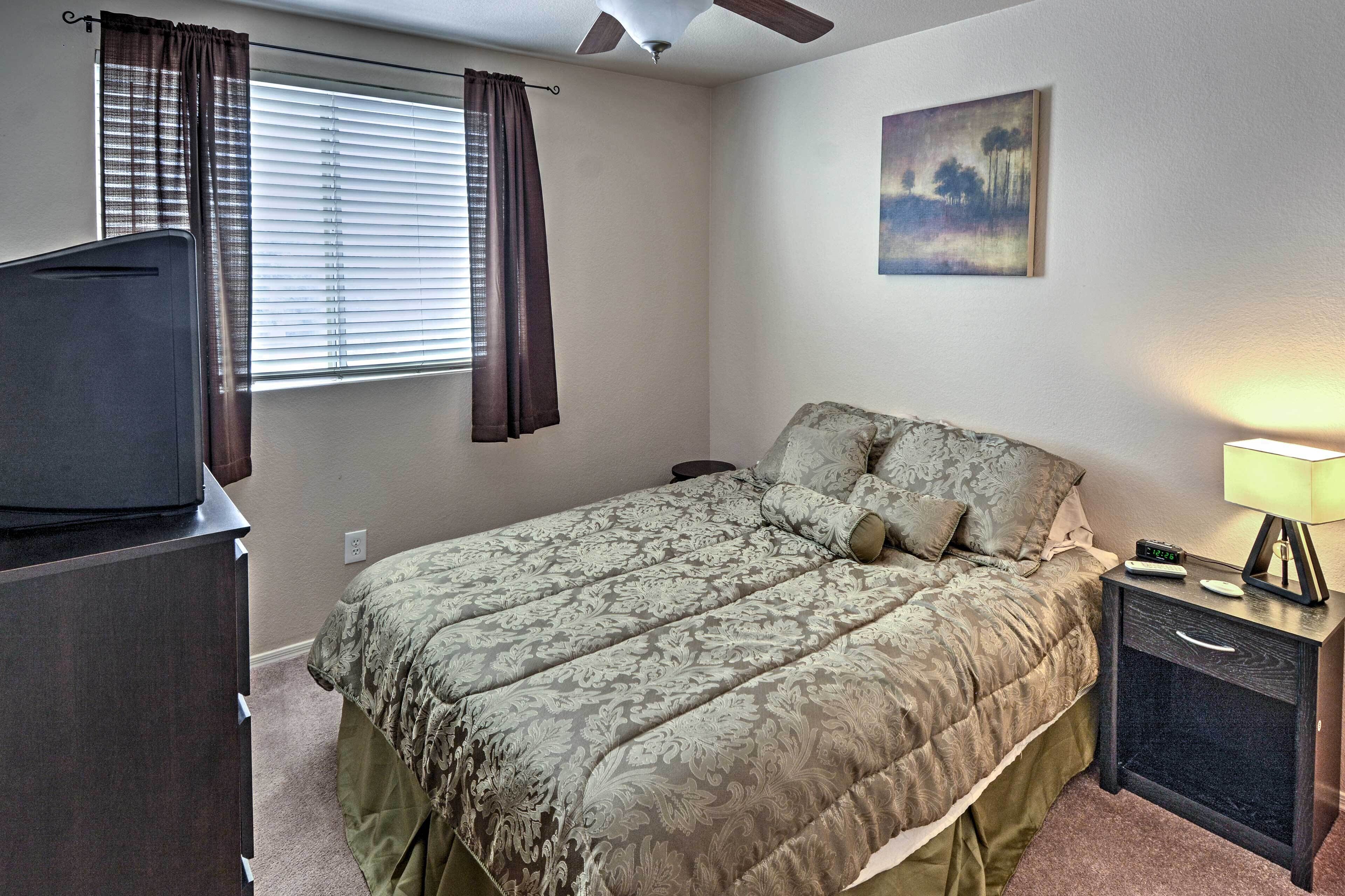 A bedroom with a bed, a nightstand, a lamp, a television, and a window with curtains.
