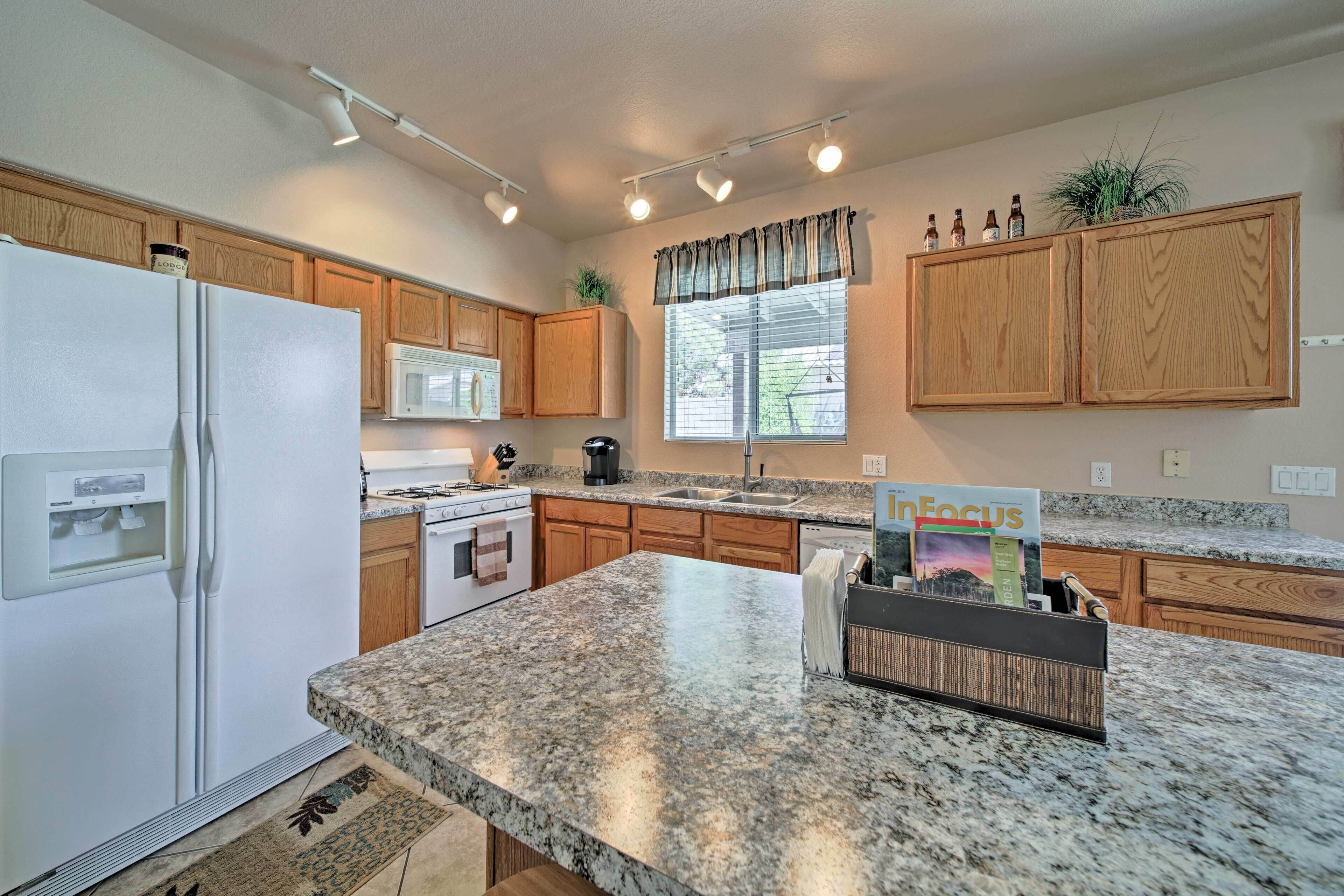 A kitchen with granite countertops, wooden cabinets, a refrigerator, a microwave, and a window with curtains.
