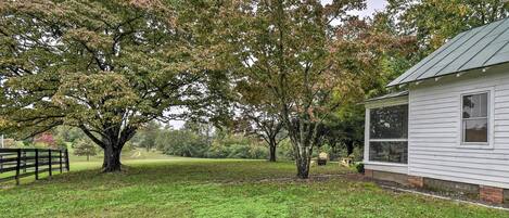 A white house with a green roof, surrounded by a grassy yard and large trees.