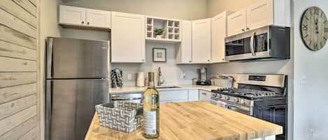 A modern kitchen with white cabinets, a stainless steel refrigerator, a wooden countertop, a wine bottle, and a clock on the wall.