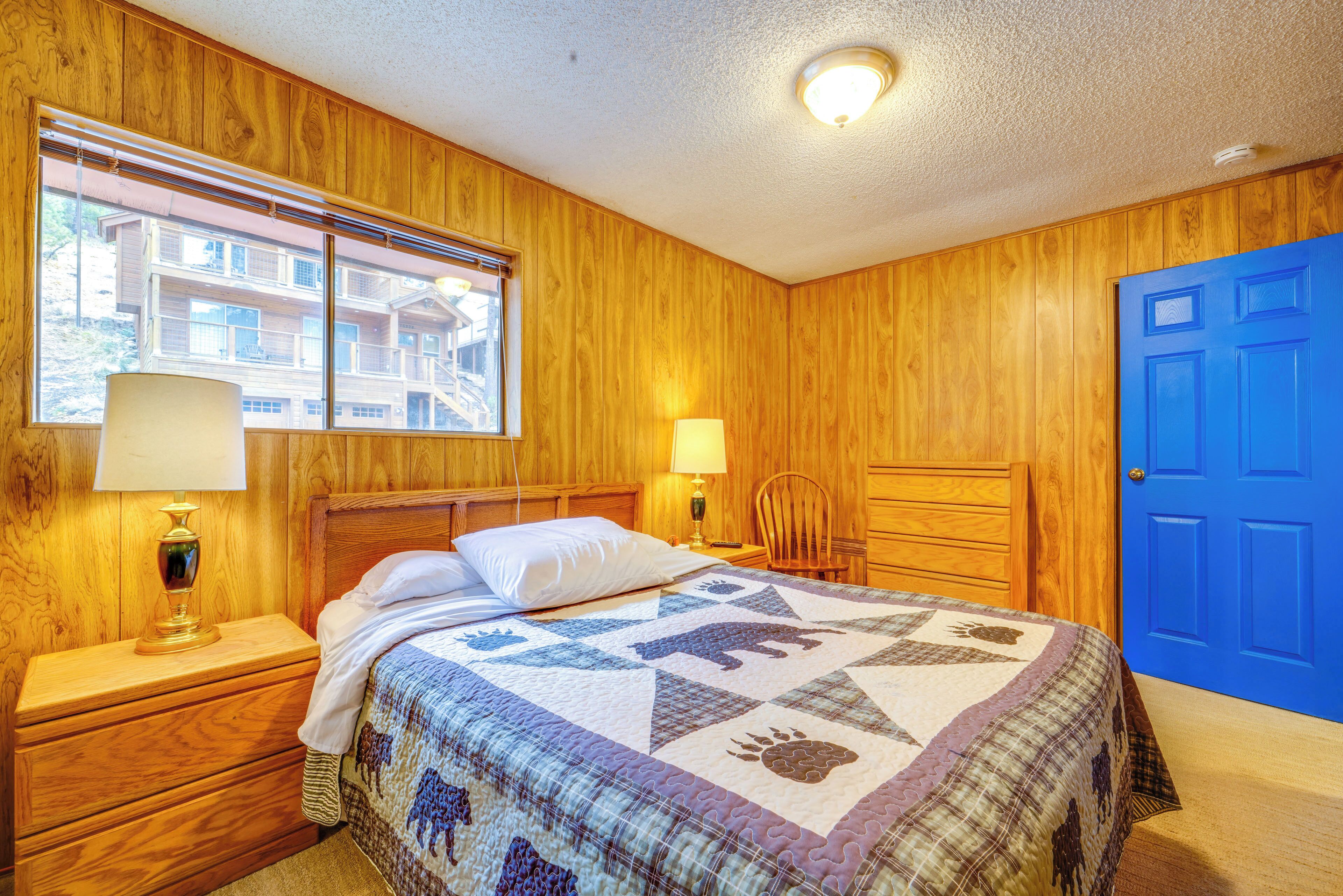 Ein Schlafzimmer mit einer Holzwand, einer blauen Tür, einem Bett mit einer Steudecke, einem Nachttisch mit einer Lampe und einem Fenster mit Jalousien.