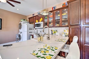 A kitchen with wooden cabinets, a microwave, a washing machine, and a dining area with a table and chairs. - Modern Sun City Studio Near Deer Valley Golf (Sun City West)