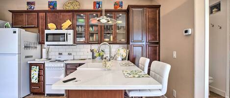 Cocina moderna con una isla central, armarios de madera, un refrigerador de acero inoxidable, un microondas y una estufa.