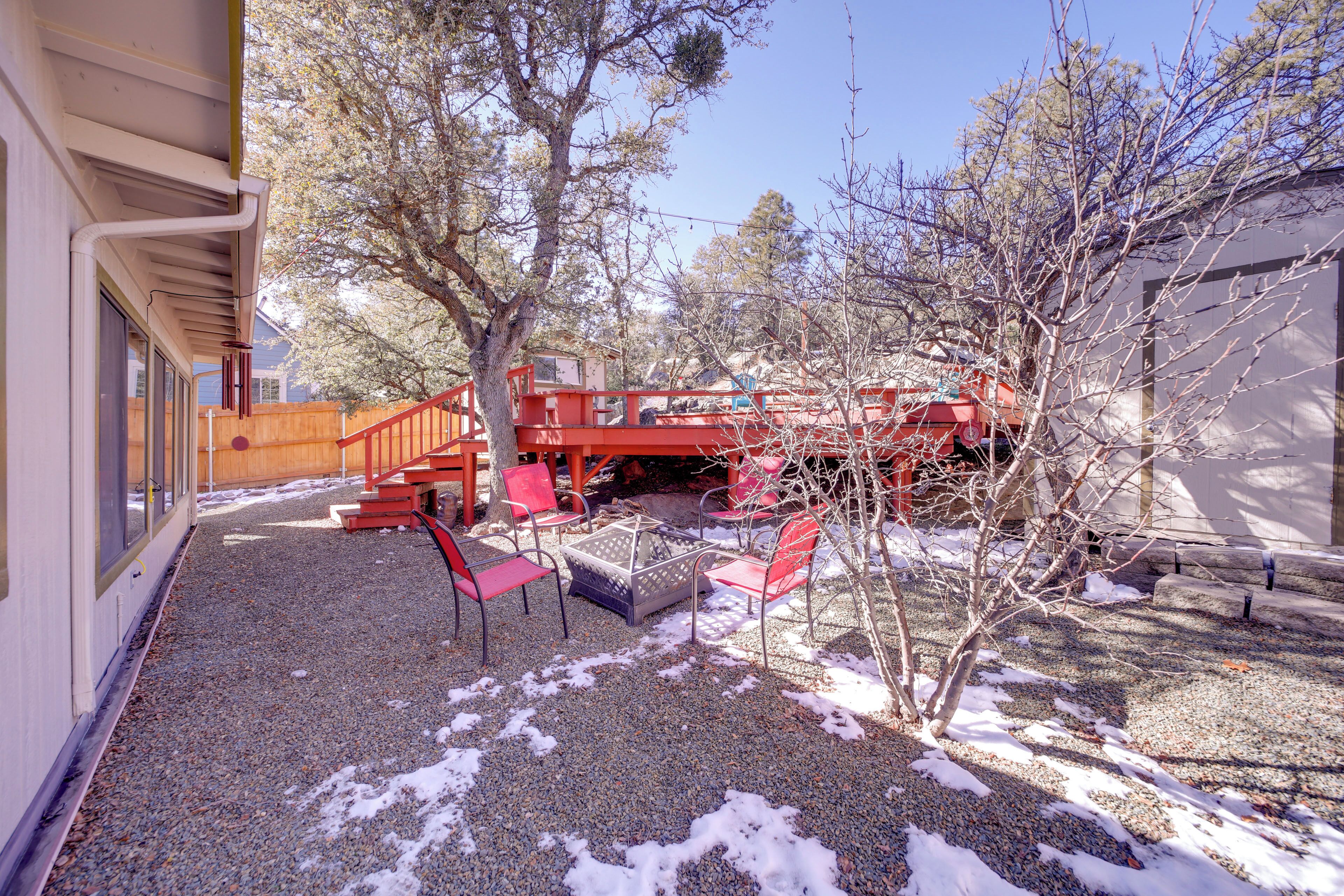 A covered outdoor area with red chairs and a table, gravel ground, and a wooden fence.