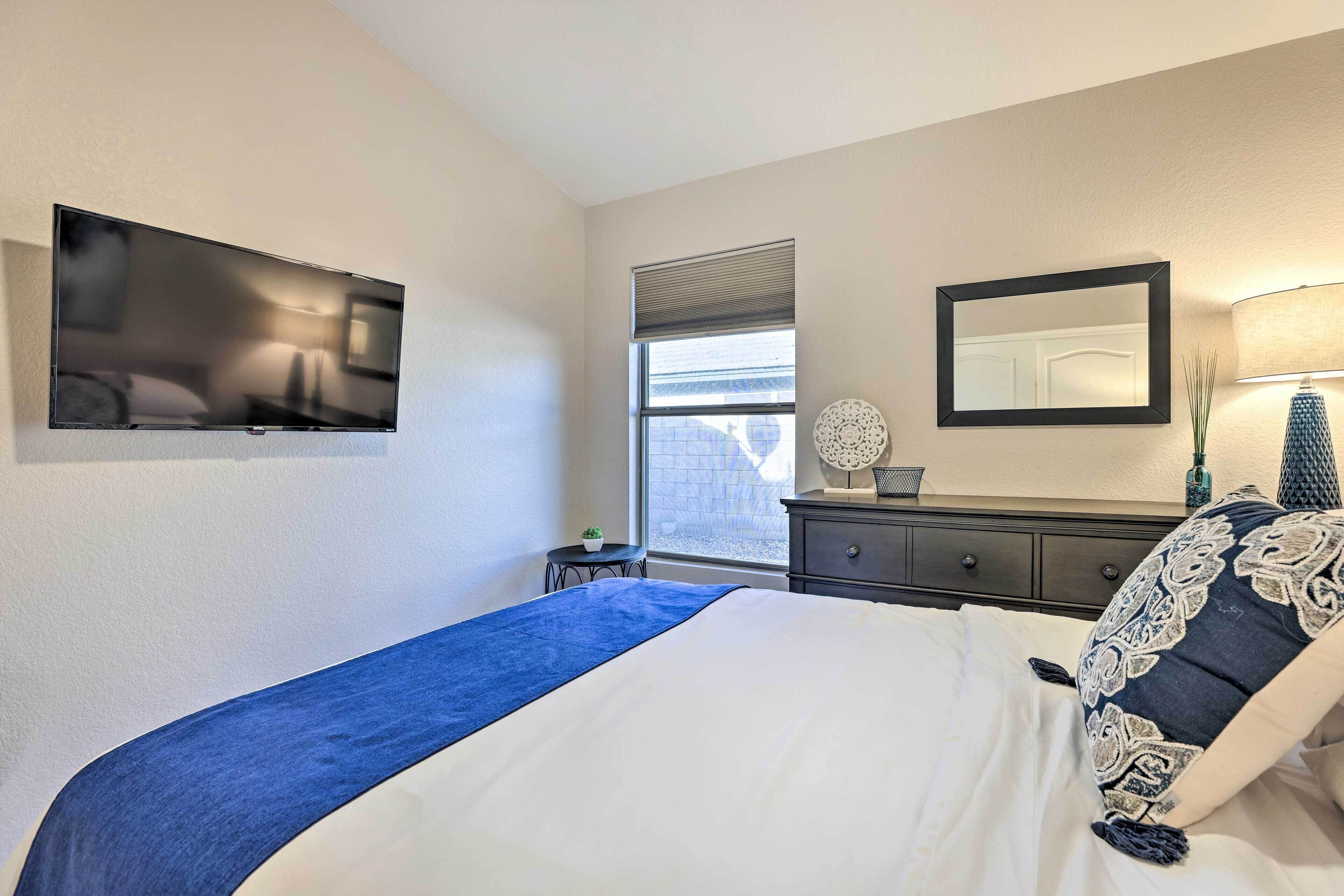 Une chambre d’hôtel comprenant un lit, un téléviseur fixé au mur, une fenêtre avec des stores, une commode et un miroir.