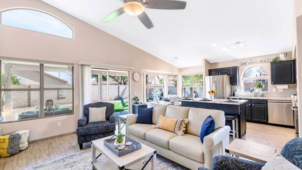 A spacious living room with a large sofa, a coffee table, and a dining area with a kitchen in the background. - Close to Spring Training! Serene Retreat in Gibert (Gilbert)