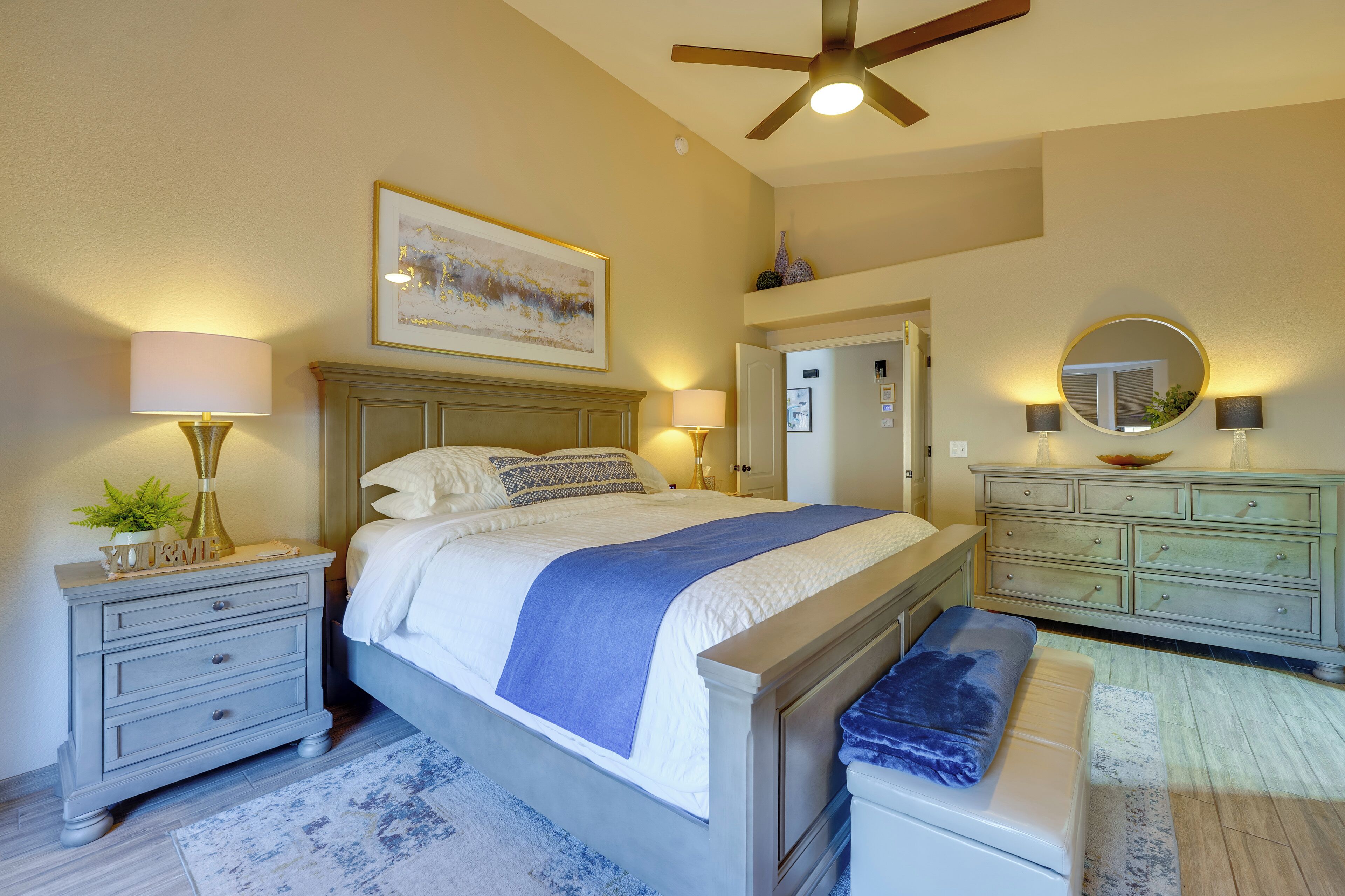 A bedroom with a bed, nightstands, a dresser, a ceiling fan, and a painting on the wall.