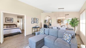 A modern living room with a grey sectional sofa, a bed with a blue and white bedspread, and a small side table with a plant. - Close to Spring Training! Serene Retreat in Gibert (Gilbert)