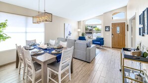 A modern living room with a grey sectional sofa, a dining table set for four, and a hanging light fixture. - Close to Spring Training! Serene Retreat in Gibert (Gilbert)